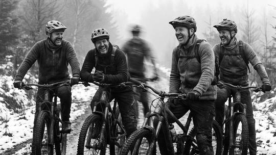 four muddy riders stopped side by side on a misty fire road, laughing