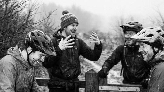 four riders regrouping at a wooden field gate, mid-story