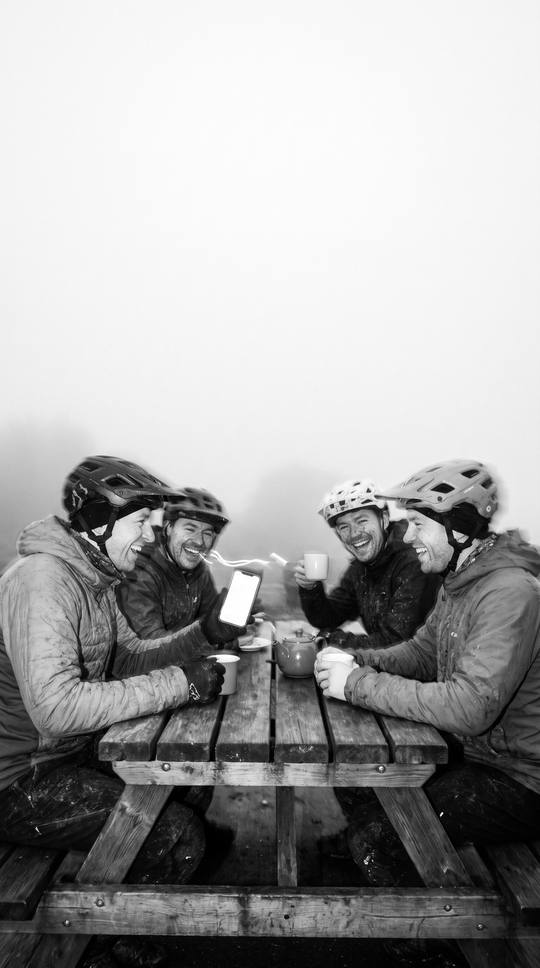 riders leaning in over a phone at a café table