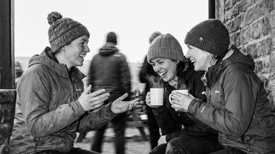three riders in beanies with mugs of tea on a stone porch bench